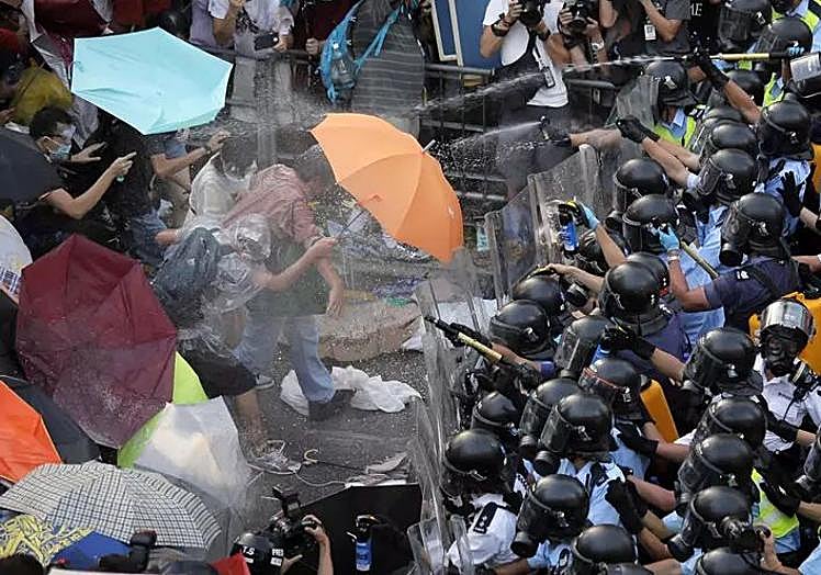 Manifestantes se protegen con sus paraguas de los ataques con gas lacrimógeno de la policía.